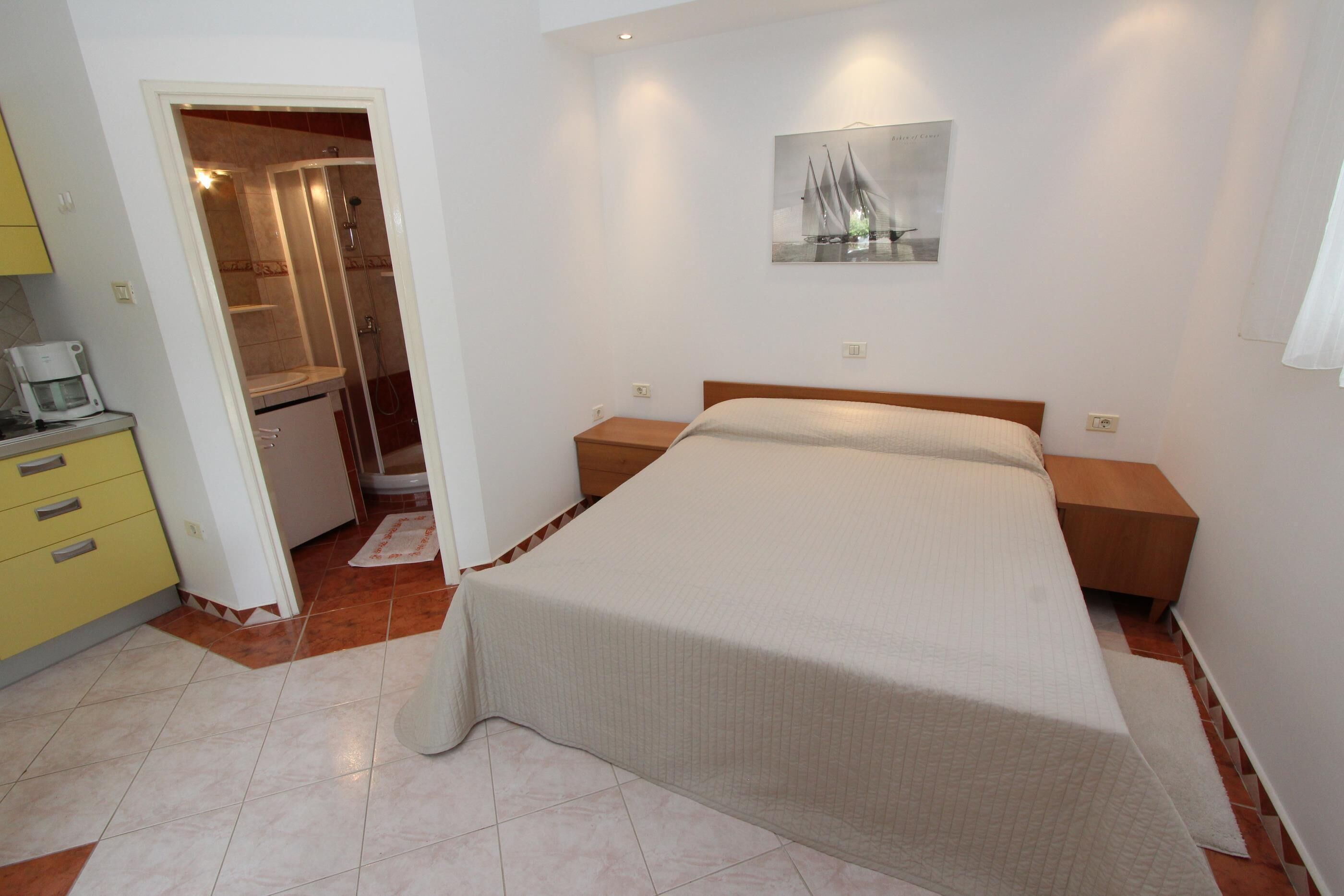Un dormitorio con cama, mesitas de noche, un cuadro y un baño con ducha.