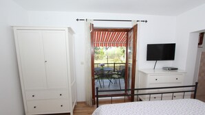 Un dormitorio con cama, armario, televisor y balcón con mesa y sillas.
