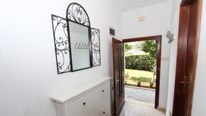 Un pasillo con un aparador blanco, un espejo con marcos decorativos y una puerta que da a un espacio exterior con jardín.