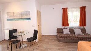 En stue med et glasbord, to sorte stole, en brun sofa med hvide puder og et vindue med orange gardiner.