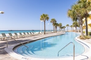 Piscina con una profundidad máxima de 0.9 metros, rodeada de palmeras y sillas de descanso, con una playa y muelle al fondo.