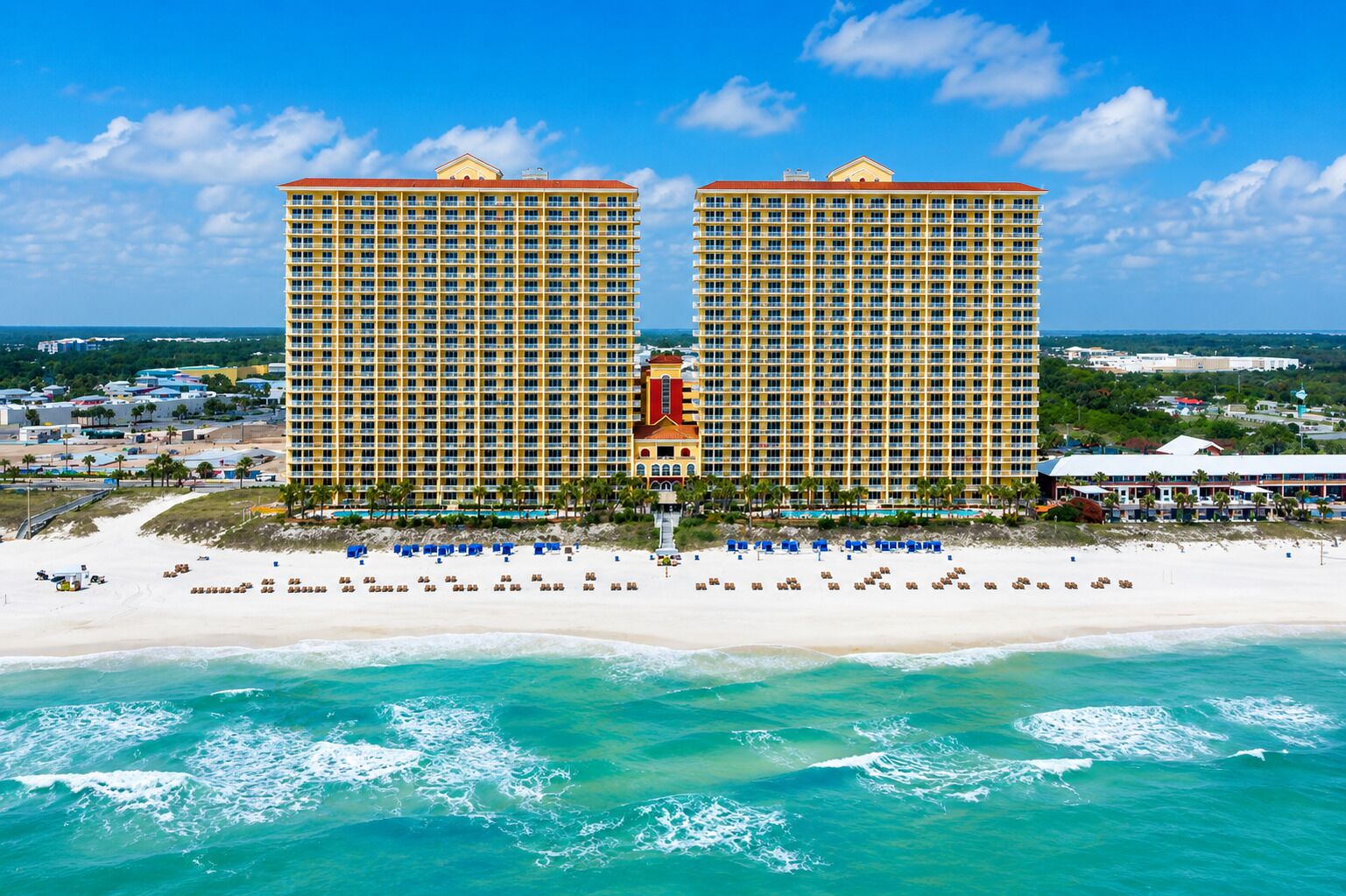 Un hotel frente a la playa con dos edificios destacados, una playa de arena y vistas al océano.