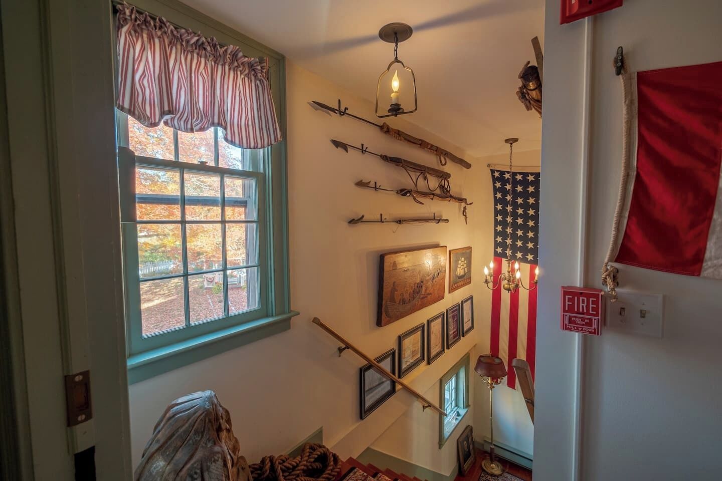 A room with a window, a staircase, and a wall decorated with various items including a flag, framed pictures, and a fire alarm.