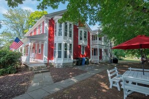 A red and white colonial-style house with a porch, a flag, and outdoor seating. - 1784 Denison Home~ New England Nautical Inspiration~ Welcome to Warm Hospitality (Stonington)