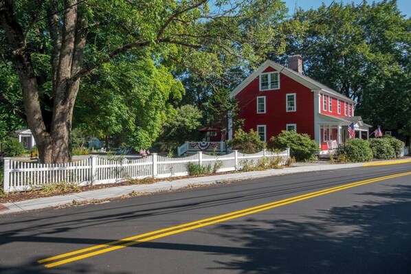 A red house with a white picket fence, a clear road, and trees. - 1784 Denison Home~ New England Nautical Inspiration~ Welcome to Warm Hospitality (Stonington)