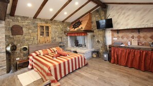 A rustic room with a stone fireplace, a bed with striped bedding, a wooden ceiling, and a kitchen area with a TV. - MIDEA 2 Comfort Studio with Terrace 5 (Rovinjsko Selo)