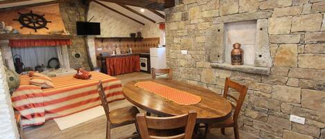 A cozy room with a wooden dining table, two chairs, a stone fireplace, and a kitchen area with a stove and sink.