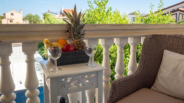 A balcony with a wicker chair and a small table holding a fruit basket and two wine glasses. - DOMIC Studio Apartment 1 (Banjole)