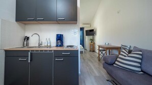 A compact kitchen with dark cabinets, a coffee maker, and a dishwasher. There is a small dining area with a table and a sofa with striped cushions. - DOMIC Studio Apartment 1 (Banjole)