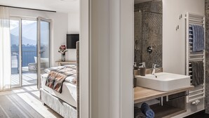 Moderni hotellihuone, jossa on parveke, suuri sänky, suihkulla varustettu kylpyhuone ja näkymä vuorille.
