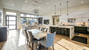 A modern kitchen with a central island, a dining area with a large table and chairs, and a view of the outdoors through large windows. - Scottsdale Walk to Old Town - 4BR Luxury Villa w/ Pool, Spa & Fire Pit (Scottsdale)