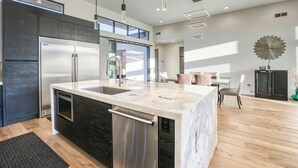 A modern kitchen with a marble island, stainless steel appliances, and a dining area with wooden flooring and a large decorative wall piece. - Scottsdale Walk to Old Town - 4BR Luxury Villa w/ Pool, Spa & Fire Pit (Scottsdale)