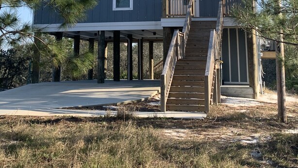 Een huis met twee verdiepingen, een overdekte veranda en een houten trap naar een terras.