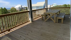 Een houten terras met een tafel en banken, met uitzicht op een kustgebied met huizen en bomen.