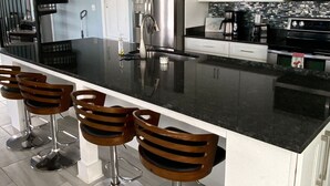 Een moderne keuken met een centraal kookeiland, roestvrijstalen apparatuur en een zwart aanrecht.