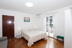 A bedroom with a bed, a nightstand, a green bench, a door, and a window with curtains.