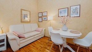 A living room with a white sofa, a dining table with chairs, and framed pictures on the wall. - VILLA ROSSELLA 2 Studio (Eufemia) (Rovinj)