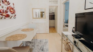 A modern living room with a TV, a dining table with placemats, and a kitchen in the background. - VILLA ROSSELLA 2 Studio (Cardaria) (Rovinj)