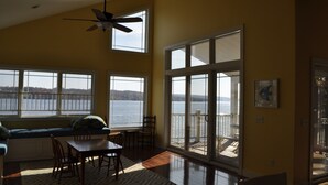 A spacious room with large windows overlooking a body of water, a ceiling fan, and a dining area with a table and chairs.
