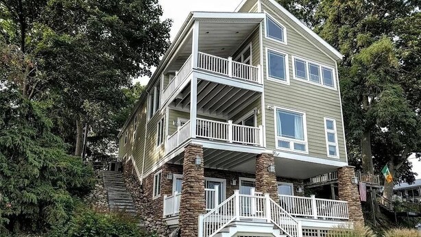 A multi-story house with a stone foundation, a balcony on the second floor, and a porch with steps leading to the entrance.