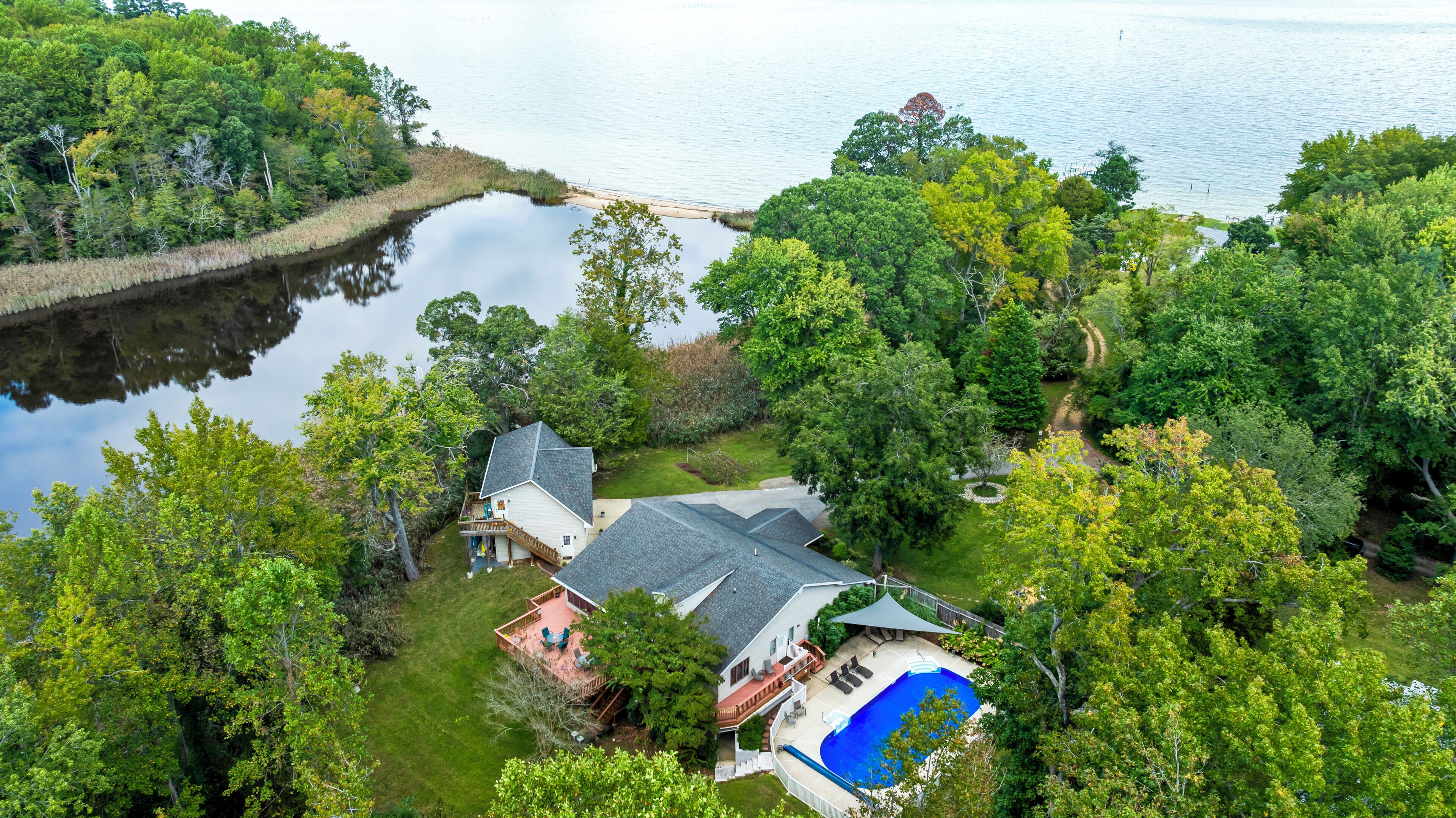 Une maison avec une piscine, entourée d’une forêt dense et bordée d’un lac.