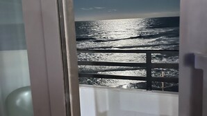 Vista del océano desde un balcón con barandilla, una luna en el cielo y un marco de puerta al frente.