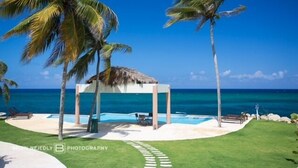 Ein Resort am Strand mit Pool, Palmen und einem Gazebo mit Reetdach.