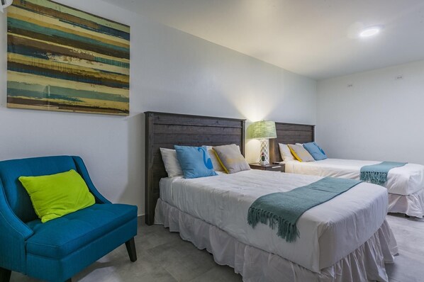 Une chambre d’hôtel avec deux lits, un fauteuil bleu et un tableau au mur.