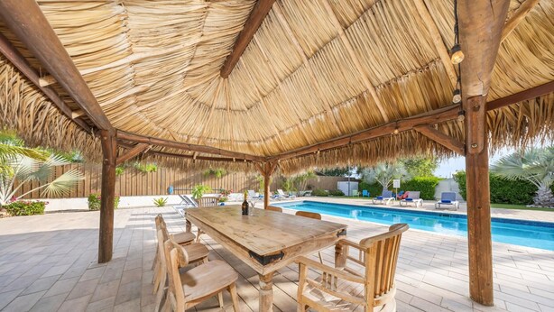 Una terraza de madera con techo de paja, piscina y sillas de descanso.