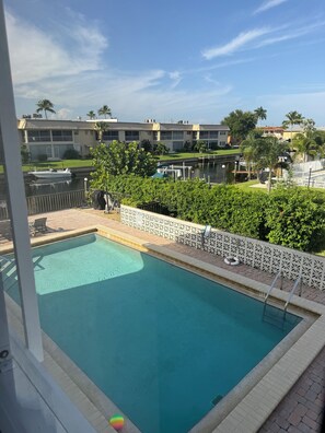 A swimming pool with a view of a residential area, including a boat dock and a building with a balcony.