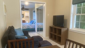 Een kleine zithoek met een bank, een voetenbankje, een houten tafel en een televisie op een standaard.