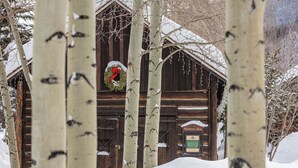 A wooden cabin with a sign reading "Frisco Jail" amidst snow-covered trees.