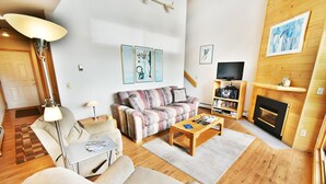 A cozy living room with a sofa, armchairs, a coffee table, a fireplace, and a TV.
