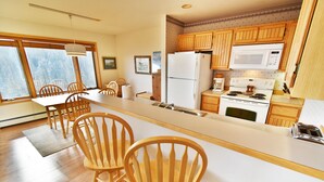 A kitchen with wooden cabinets, a white refrigerator, a microwave, and a stove. There are wooden chairs around a table.