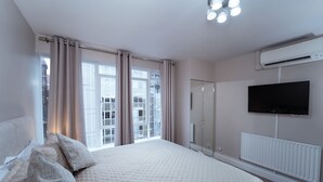 Een slaapkamer met een groot bed, een kledingkast, een aan de muur bevestigde televisie en een raam met gordijnen.