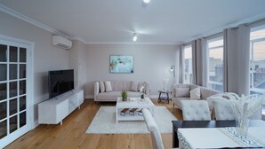 Een moderne woonkamer met een flatscreen televisie, twee banken, een salontafel en een eethoek met een tafel en stoelen.