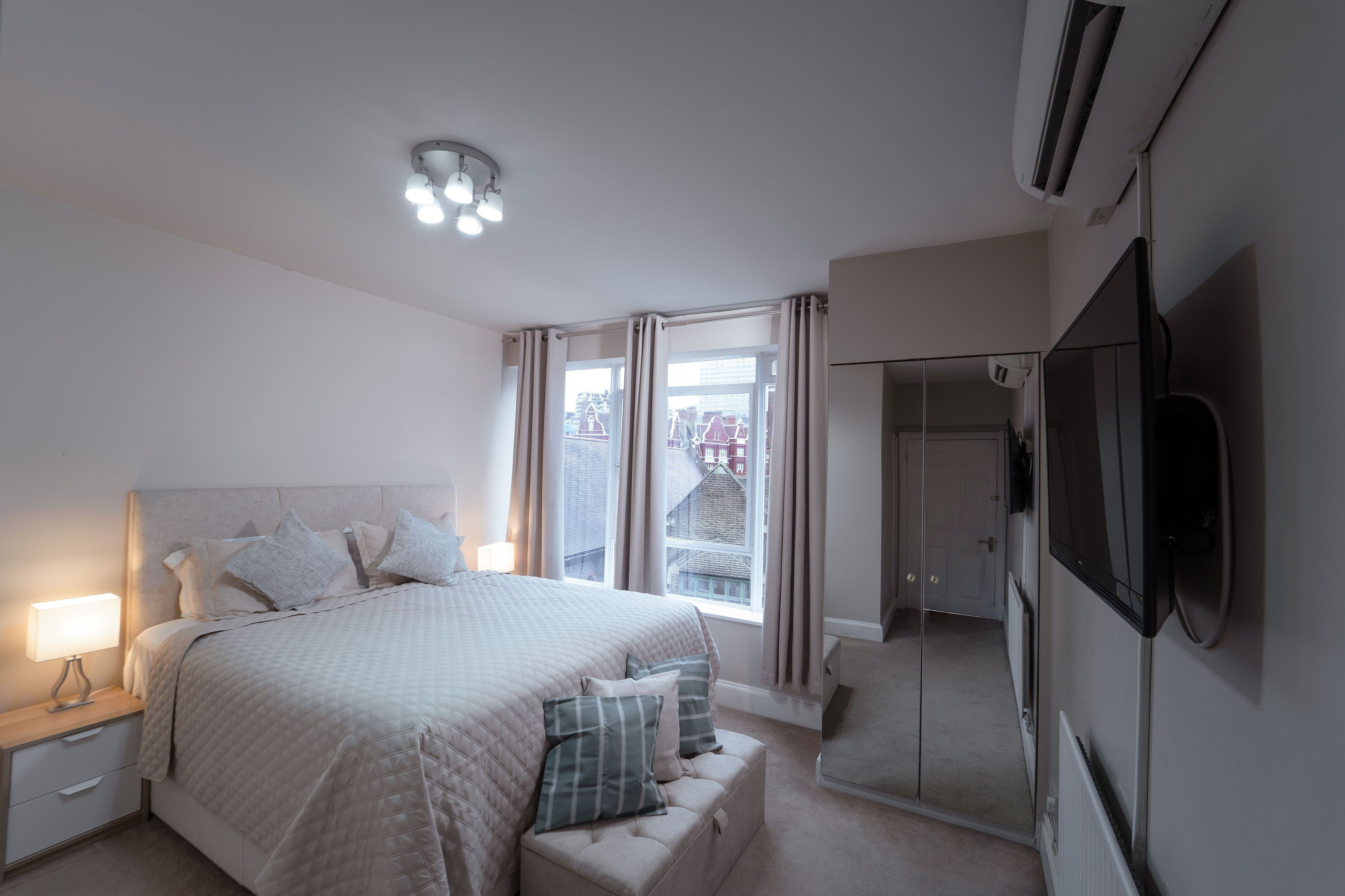A bedroom with a bed, bedside table, lamp, and a TV mounted on the wall.