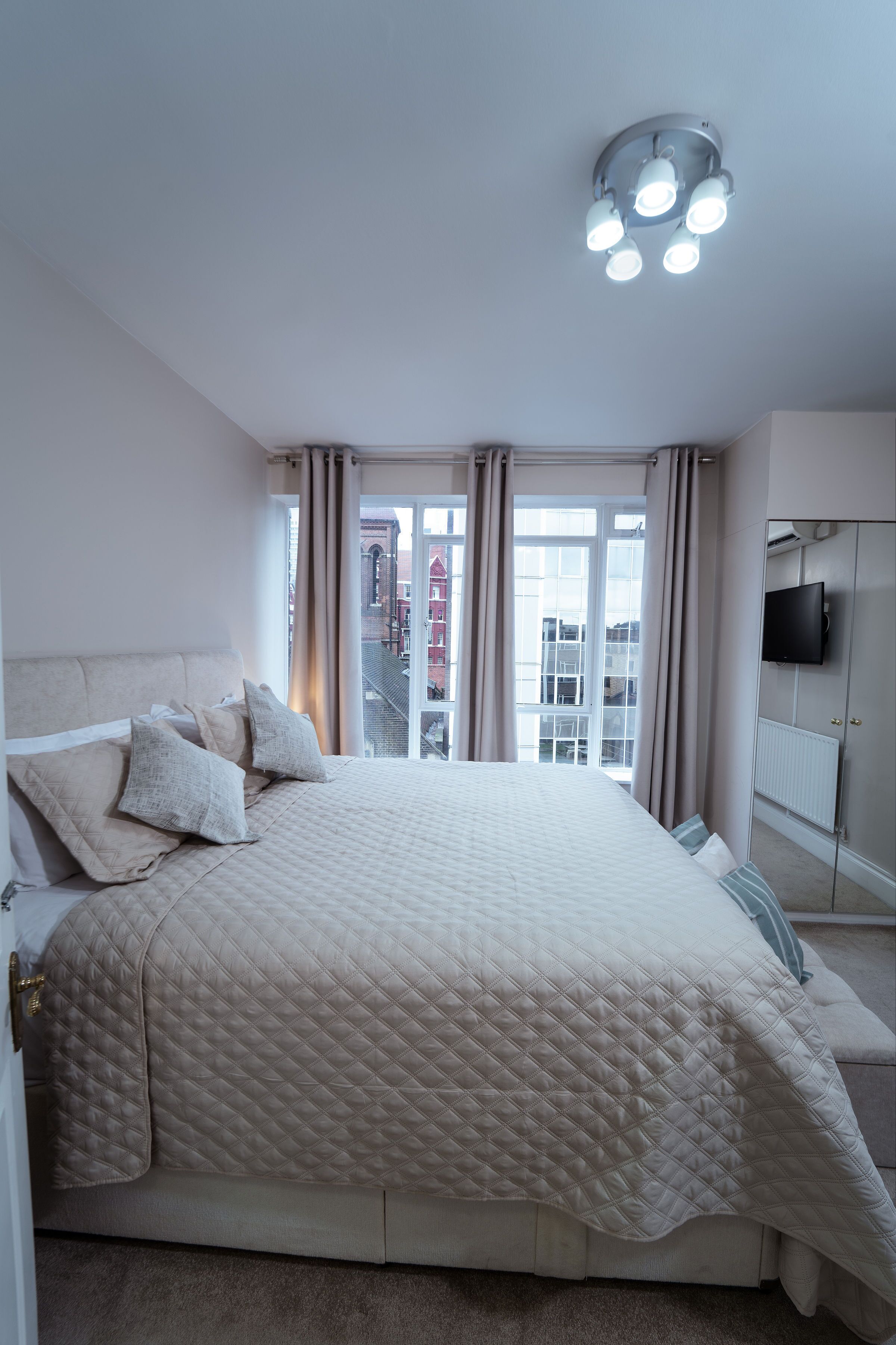 Een slaapkamer met een groot bed, een televisie aan de muur en uitzicht op gebouwen.