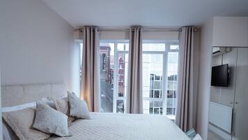 Een slaapkamer met een groot bed, een televisie aan de muur en uitzicht op gebouwen.