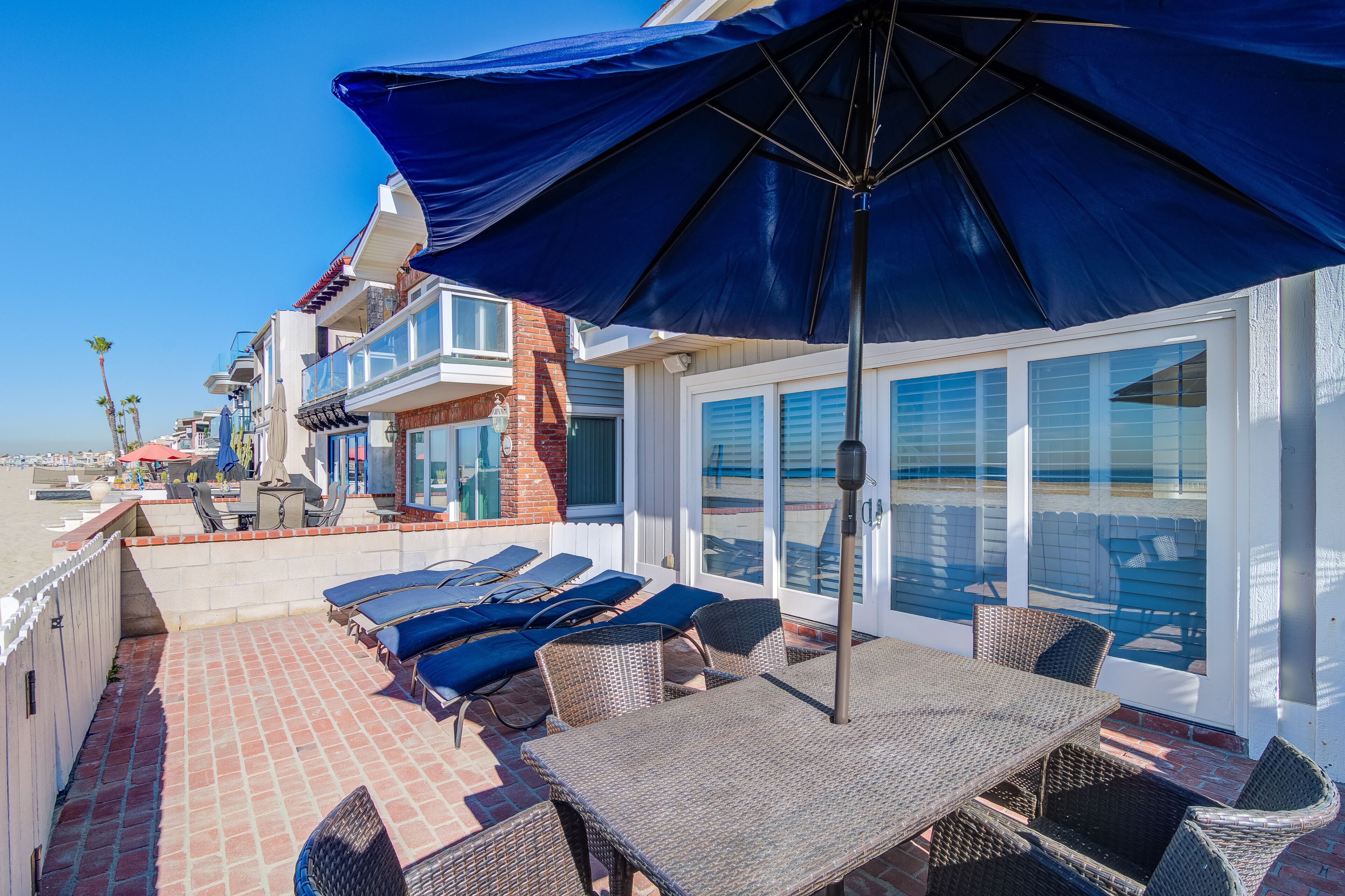 A rooftop patio with outdoor furniture, a large umbrella, and a view of the beach.