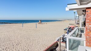 A beach view with a lifeguard tower, a patio with outdoor seating, and a clear blue sky.
