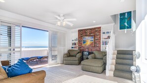 A spacious living room with a large sliding glass door leading to a balcony, a ceiling fan, and a brick accent wall.