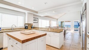 A spacious kitchen with white cabinetry, a large island with a wooden countertop, and a view of the ocean through the sliding glass doors.