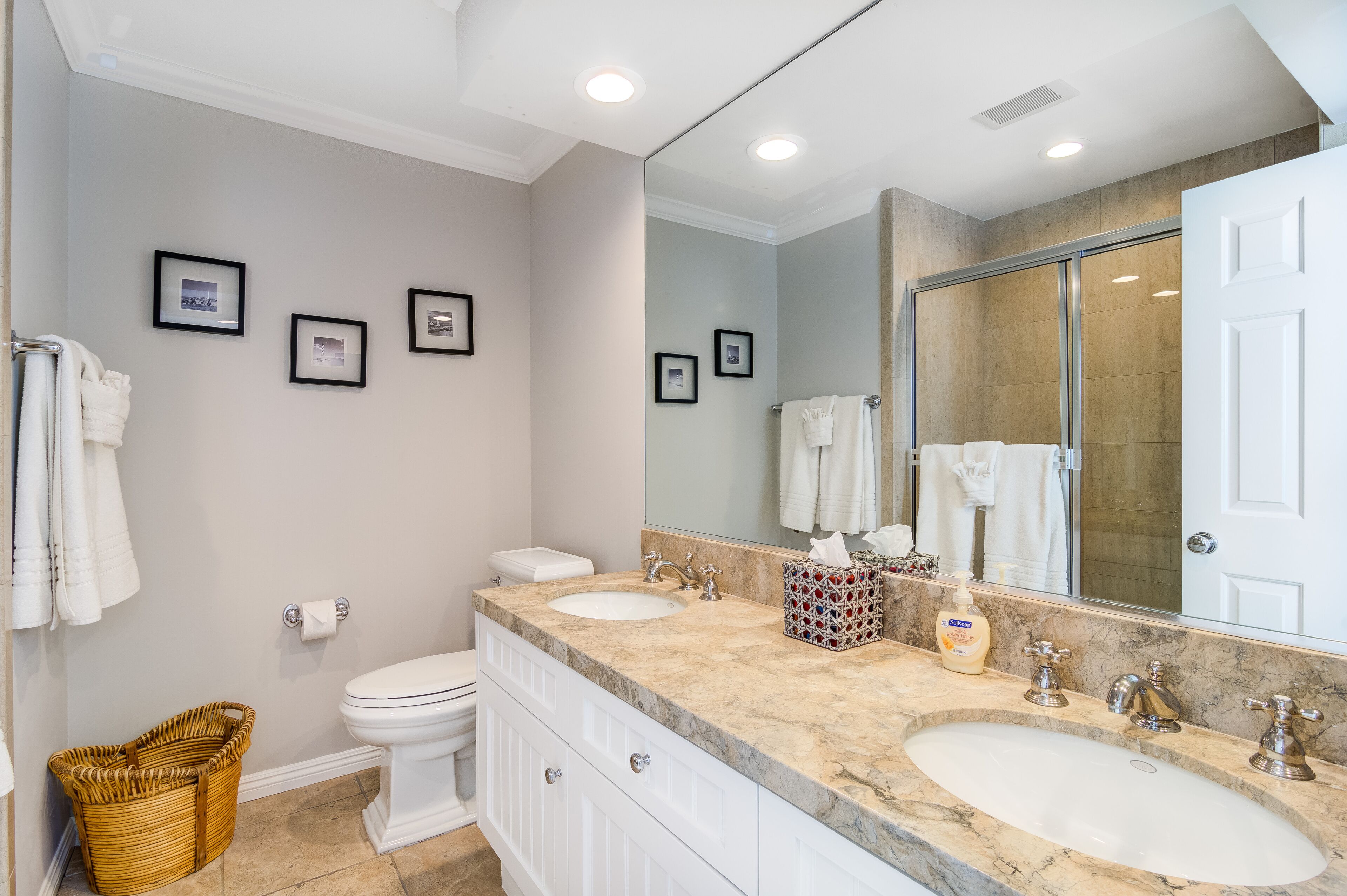 A modern bathroom with a large mirror, two sinks, a toilet, and framed pictures on the wall.