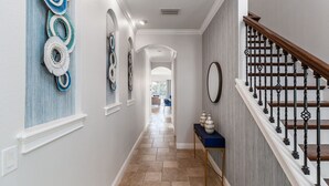 A hallway with a staircase, decorative wall art, and a console table with vases. - Paradise Point | 5 Bed, 5.5 Bath Luxury Villa with Private Pool, Galaxy Arcade (Kissimmee)