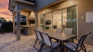 Um pátio externo com mesa e cadeiras, uma porta de vidro que dá para um quarto e uma placa indicando serviço de aluguel de piscina.