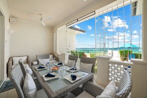 A sunlit patio with a glass table set for dining, wicker furniture, and a view of the sea. - Paradise Villa (St James)