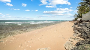 Una platja amb aigua cristal·lina, sorra daurada i un mur rocos amb vegetació.