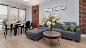 A modern living room with a grey sofa, round coffee table, and a dining area with a table and chairs. - Stylish Apartment with Parking | Air Conditioning | Near the Market Square (Poznań)