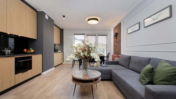 A modern kitchen with wooden cabinets, a dining area with a table and chairs, and a grey sofa with green cushions. - Stylish Apartment with Parking | Air Conditioning | Near the Market Square (Poznań)